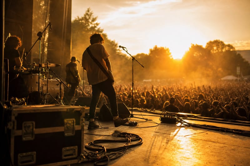 Editorial photo: a touring band loading merchandise boxes and gear into a van outside a small venue at dusk, no readable text