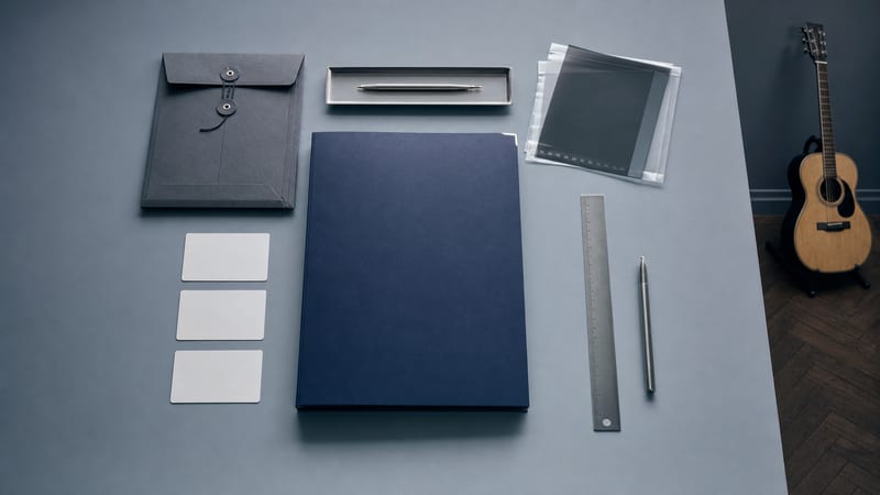 Cool overhead desk with a closed navy folder, blank credit cards, ruler, pen, and a small intact acoustic guitar resting at the edge.