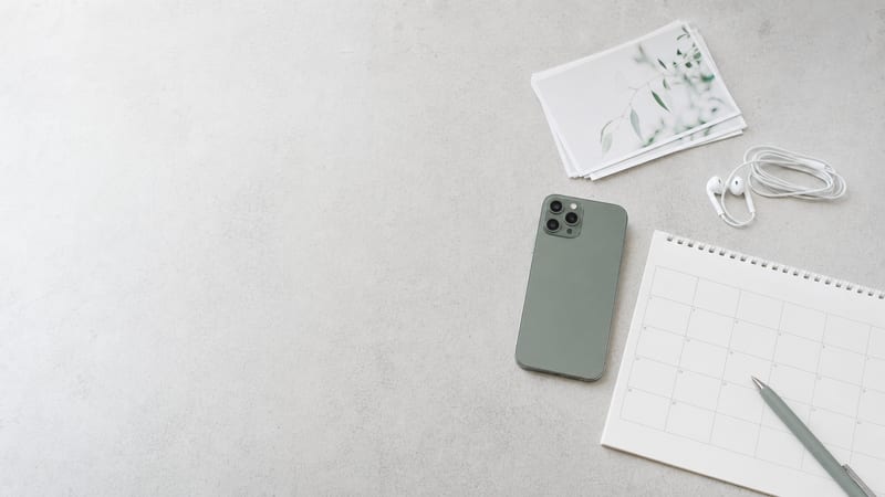 A phone resting face-down beside a blank calendar page and earbuds on a light tabletop.