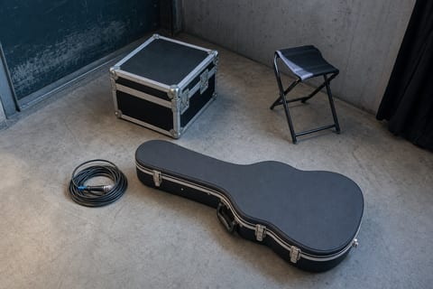 Cool blue-grey club stage with a microphone, closed folder on a stool, and electric guitar resting safely on a stand.